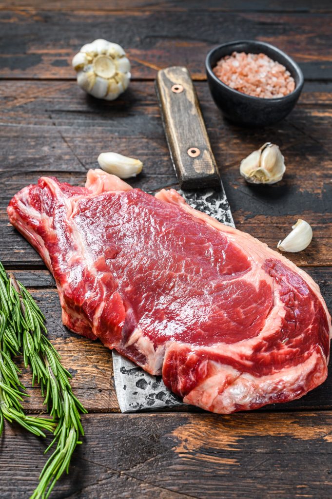 Raw cowboy or rib eye steak on the bone on a meat cleaver. Marble beef meat ribeye